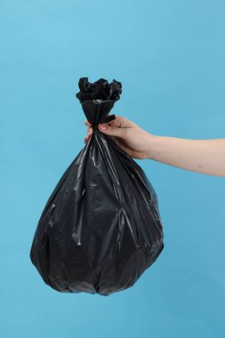 Açık mavi arka planda çöp dolu plastik poşet taşıyan kadın, yakın plan.