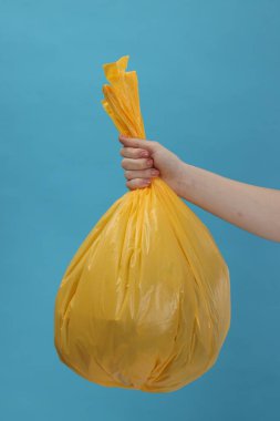 Açık mavi arka planda çöp dolu plastik poşet taşıyan kadın, yakın plan.