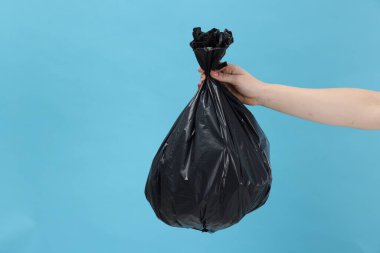 Açık mavi arka planda çöp dolu plastik poşet taşıyan bir kadın, yakın plan. Metin için boşluk