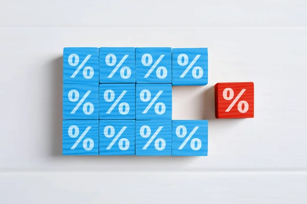 Best mortgage interest rate. Red cube with percent sign among light blue ones on white wooden table, flat lay