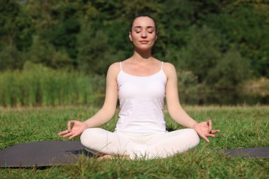 Güzel bir kadın dışarıda yoga yapıyor. Lotus pozu