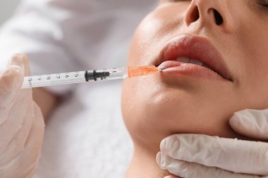 Doktor klinikteki genç bayana dudak iğnesi yapıyor, yakın plan. Estetik ameliyat