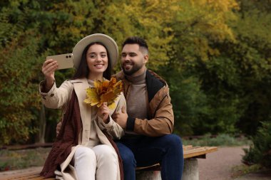 Mutlu genç çift sonbahar parkında selfie çekiyor, mesaj atmak için yer var.