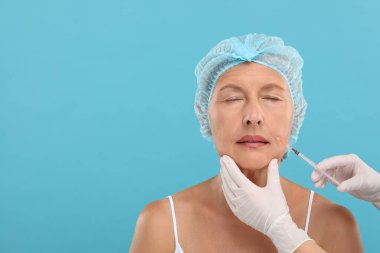 Doktor, açık mavi arka planda yaşlı kadına yüz enjeksiyonu yapıyor. Mesaj için yer var. Estetik ameliyat