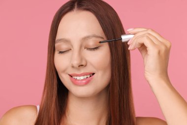 Güzel bir kadın pembe arka plandaki kirpiklere serum sürüyor.