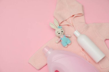 Çamaşır deterjanı şişeleri, bebek kazağı ve pembe arka planda oyuncak tavşan, düz yatak. Metin için boşluk