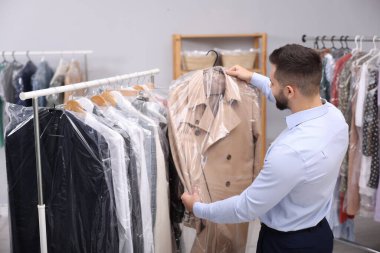 Kuru temizleme servisi. Askılık tutan bir işçi. Plastik bir çantada. Kapalı alanda giysi olan bir askıda.