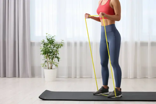 Woman doing exercise with fitness elastic band on mat at home, closeup. Space for text