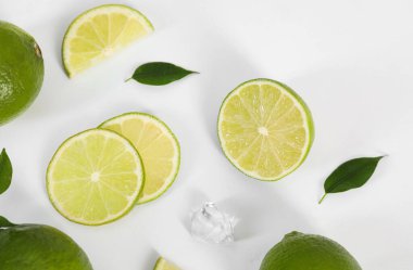 Beyaz zemin üzerinde taze limon, yaprak ve buz kübü bulunan düz bir bileşim.