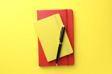Sarı arkaplanda farklı defterler ve kalem, üst görünüm