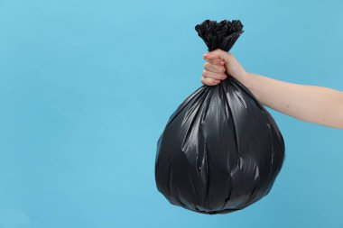 Açık mavi arka planda çöp dolu plastik poşet taşıyan bir kadın, yakın plan. Metin için boşluk