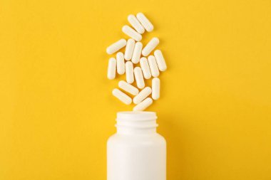 Sarı arka planda şişe ve vitamin kapsülleri, üst görünüm