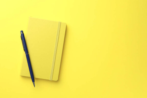 Closed notebook and pen on yellow background, top view. Space for text