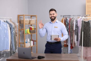 Kuru temizleme servisi. Defterli mutlu bir işçi iş yerinde iyi bir jest gösteriyor.