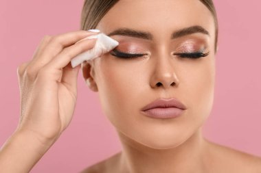 Güzel bir kadın pembe arka planda pamuklu ped ile makyajı kaldırıyor.