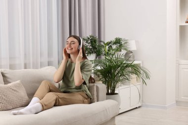 Kulaklıklı genç ve güzel bir kadın yeşil çiçekli bir kanepede müzik dinliyor.