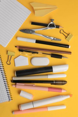 Düz kompozisyon, kağıt uçak ve turuncu arka planda farklı okul kırtasiyesi. Okula geri dön.