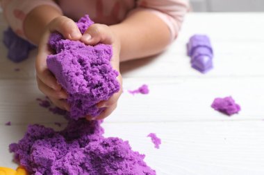 Küçük çocuk beyaz tahta masada kinetik kumla oynuyor, yakın plan.