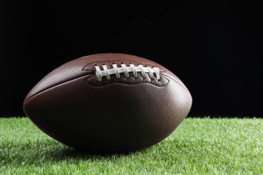 Deri Amerikan futbol topu yeşil çimlerde siyah arka planda