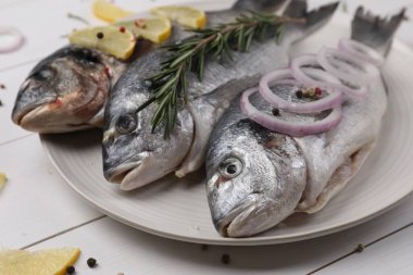 Limonlu çiğ dorado balığı, biberiye ve soğan beyaz ahşap masada, yakın plan.