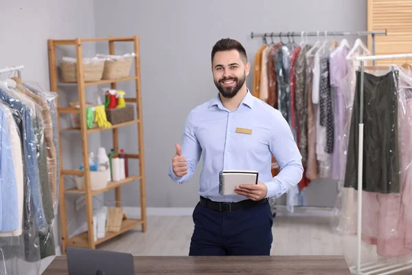 Kuru temizleme servisi. Kapalı mekanda başparmağını gösteren defterli mutlu bir işçi.