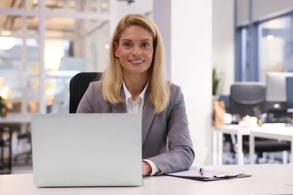Smiling woman working with laptop at table in office. Lawyer, businesswoman, accountant or manager
