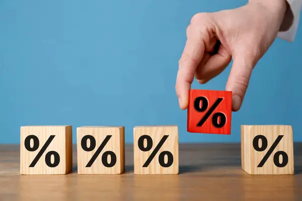 Best mortgage interest rate. Woman putting red cube with percent sign among others on wooden table, closeup