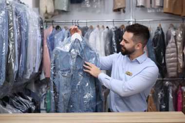 Kuru temizleme servisi. Kapalı mekanda plastik torbada kot ceketli askı tutan mutlu işçi.
