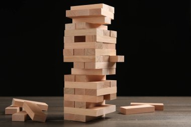 Jenga oyunu. Masanın üzerindeki tahta bloklardan yapılmış kule siyah arkaplana karşı