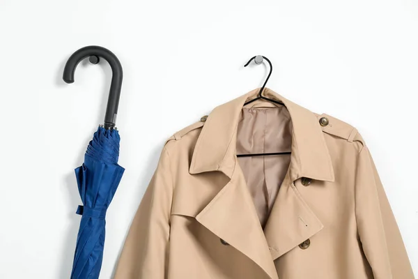 Hanger with beige trench coat and blue umbrella on white wall