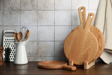 Ahşap kesme tahtaları ve mutfak aletleri fayanslı duvarın yanındaki masada.