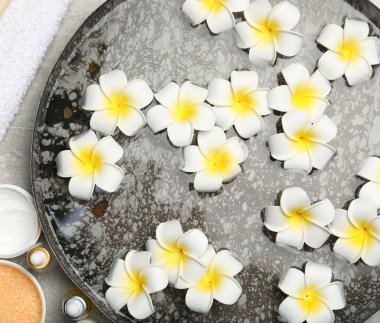 Çiçekli bir kase su ve açık gri masada farklı spa malzemeleri.