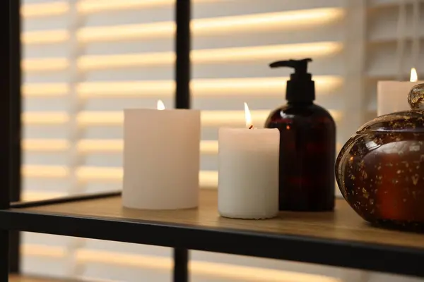 Burning candles and personal care products on shelf indoors