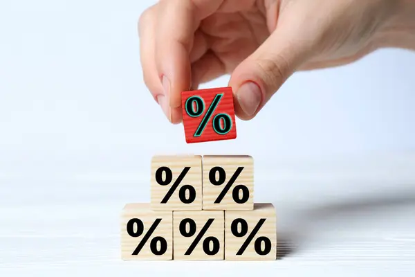 Best mortgage interest rate. Woman putting red cube with percent sign on top of pyramid of others on white background, closeup