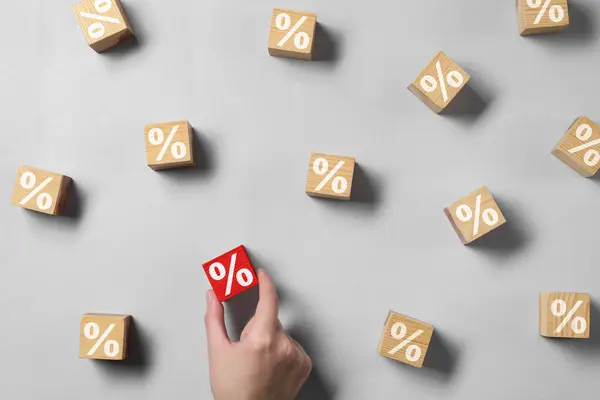 Best mortgage interest rate. Woman taking red cube with percent sign among wooden ones on light background, top view