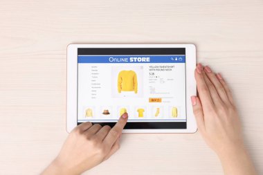 Tabletli bir kadın beyaz ahşap masada internetten alışveriş yapıyor.