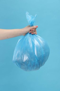 Açık mavi arka planda çöp dolu plastik poşet taşıyan kadın, yakın plan.