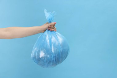 Açık mavi arka planda çöp dolu plastik poşet taşıyan bir kadın, yakın plan. Metin için boşluk