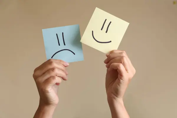 Choice concept. Woman holding papers with sad and happy emoticons on beige background, closeup