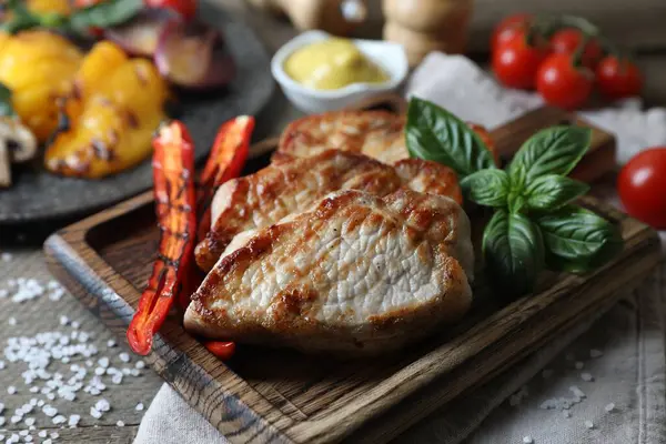 Delicious grilled meat and vegetables served on wooden table, closeup