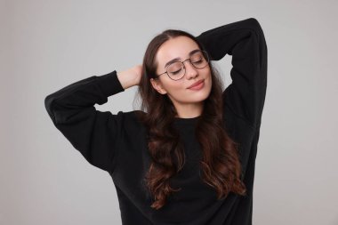 Gri arka planda, şık, sıcak süveter giyen güzel genç bir kadın.