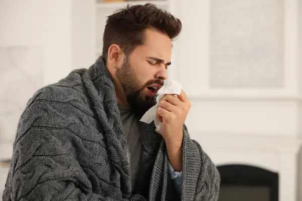 Sick man wrapped in blanket with tissue at home. Cold symptoms