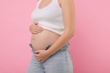 Pembe arka planda kotlu hamile kadın, yakın plan.