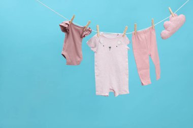 Farklı bebek kıyafetleri ve bulut şekilli yastık açık mavi arka planda çamaşır ipinde kuruyor. Metin için boşluk