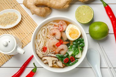 Lezzetli ramen, kasede karides ve beyaz ahşap masada malzemeler.