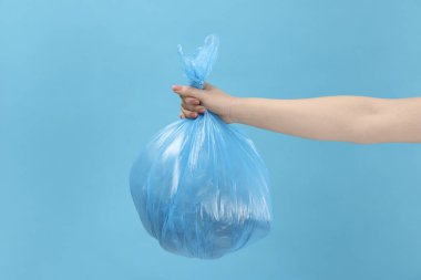 Açık mavi arka planda çöp dolu plastik poşet taşıyan kadın, yakın plan.