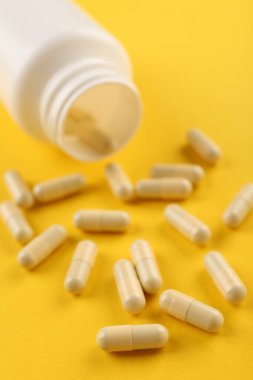 Sarı arka planda şişe ve vitamin kapsülleri, yakın plan.