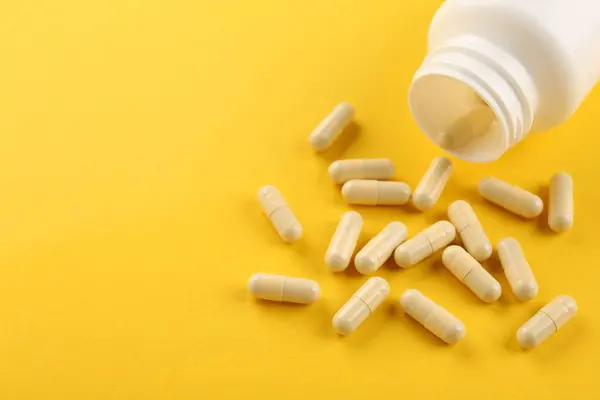 Bottle and vitamin capsules on yellow background, closeup. Space for text