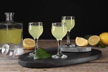 Lezzetli limoncello likörü, limon ve yeşil yapraklar ahşap masada.