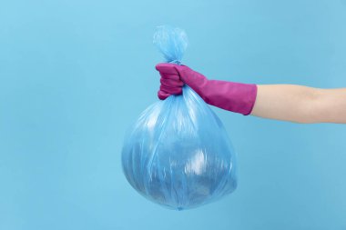 Açık mavi arka planda çöp dolu plastik poşet taşıyan kadın, yakın plan.